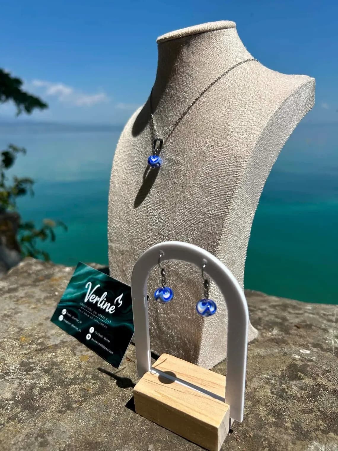 Collier et boucles d'oreilles assortis en verre filé bleu et blanc présentés face à l'eau.