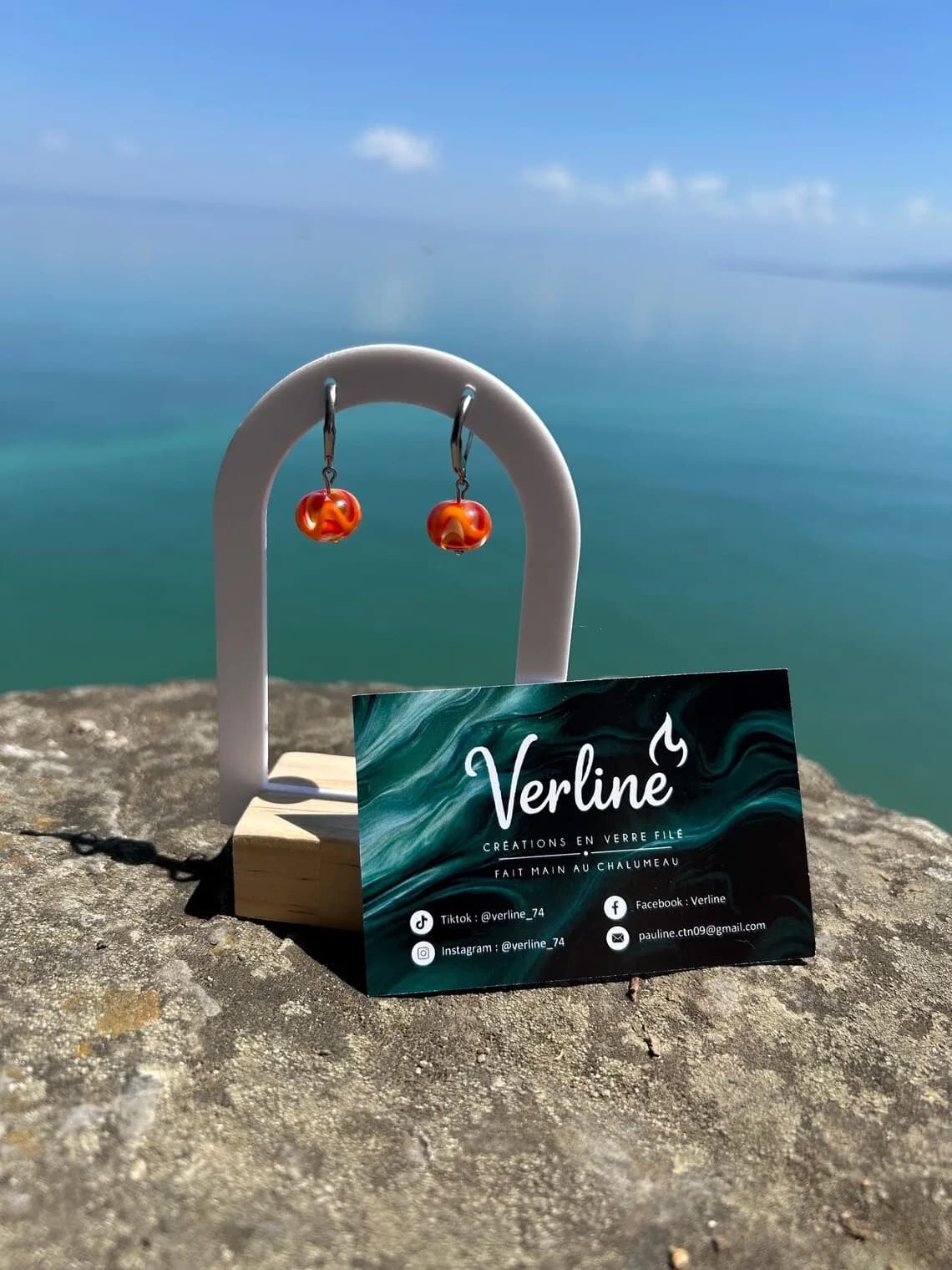 Boucles d'oreilles pendantes en verre filé ambré et orange sur créoles argentées face au lac