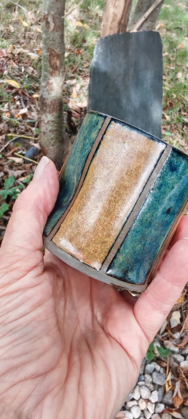 Gobelet en céramique à bandes verticales bleu, vert et ocre tenu au creux d'une main.