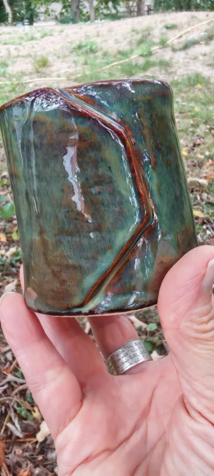 Gobelet en céramique émaillée vert et rouille tenu en main, mettant en valeur son relief plié