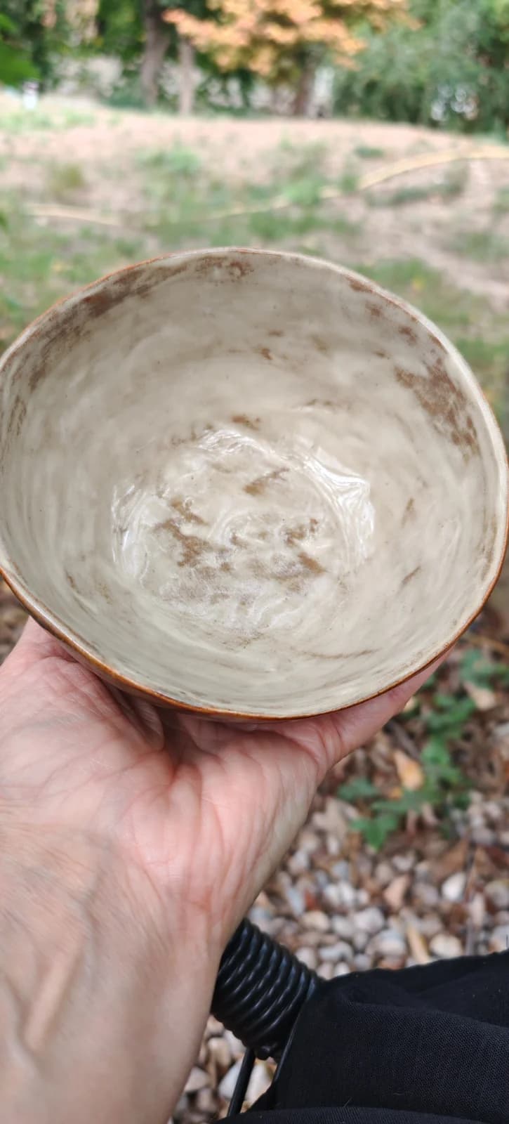 Intérieur émaillé beige marbré d'un bol artisanal en céramique tenu dans une main.