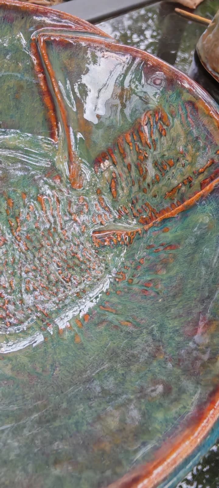 Gros plan sur l'émail vert brillant et les détails cuivrés en relief de la coupelle en céramique.