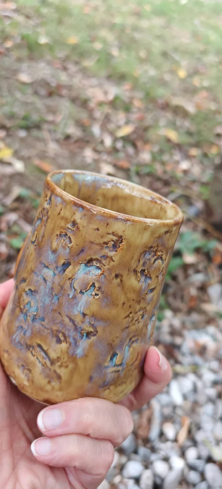 Gobelet artisanal en céramique vu de trois-quarts montrant sa texture marbrée ocre et bleutée.