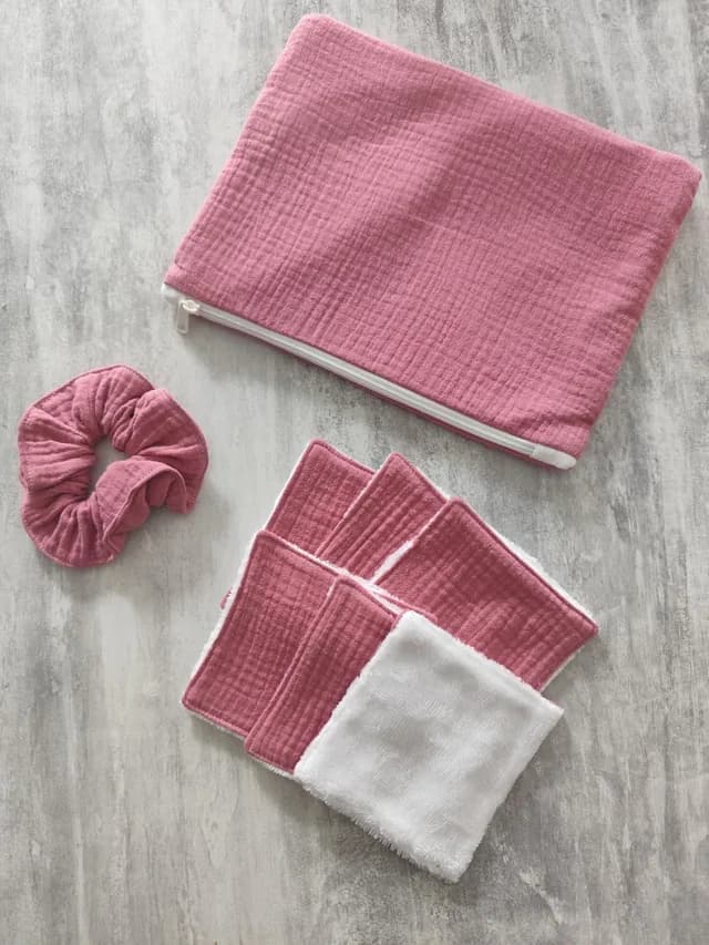 Pochette zippée rose, chouchou assorti et lingettes lavables carrées roses et blanches posés à plat.
