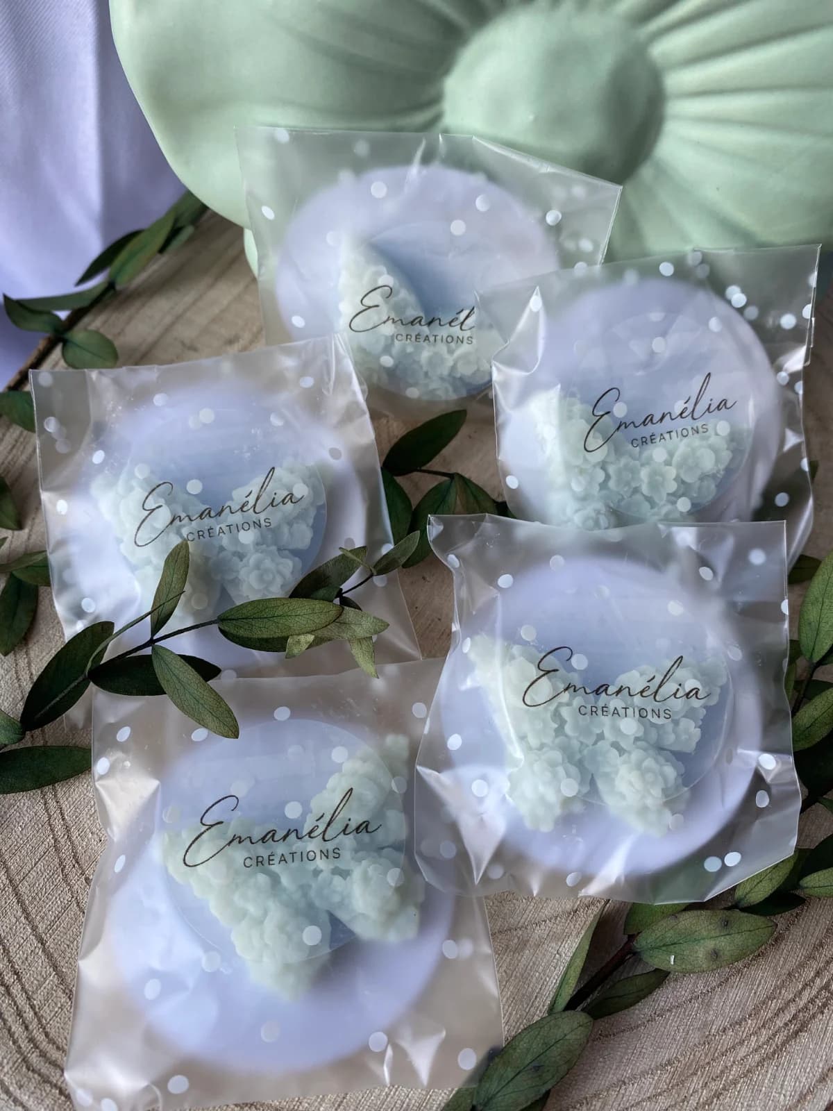 Plusieurs sachets de fondants en forme de papillon texturé entourés de feuillage vert sur bois.