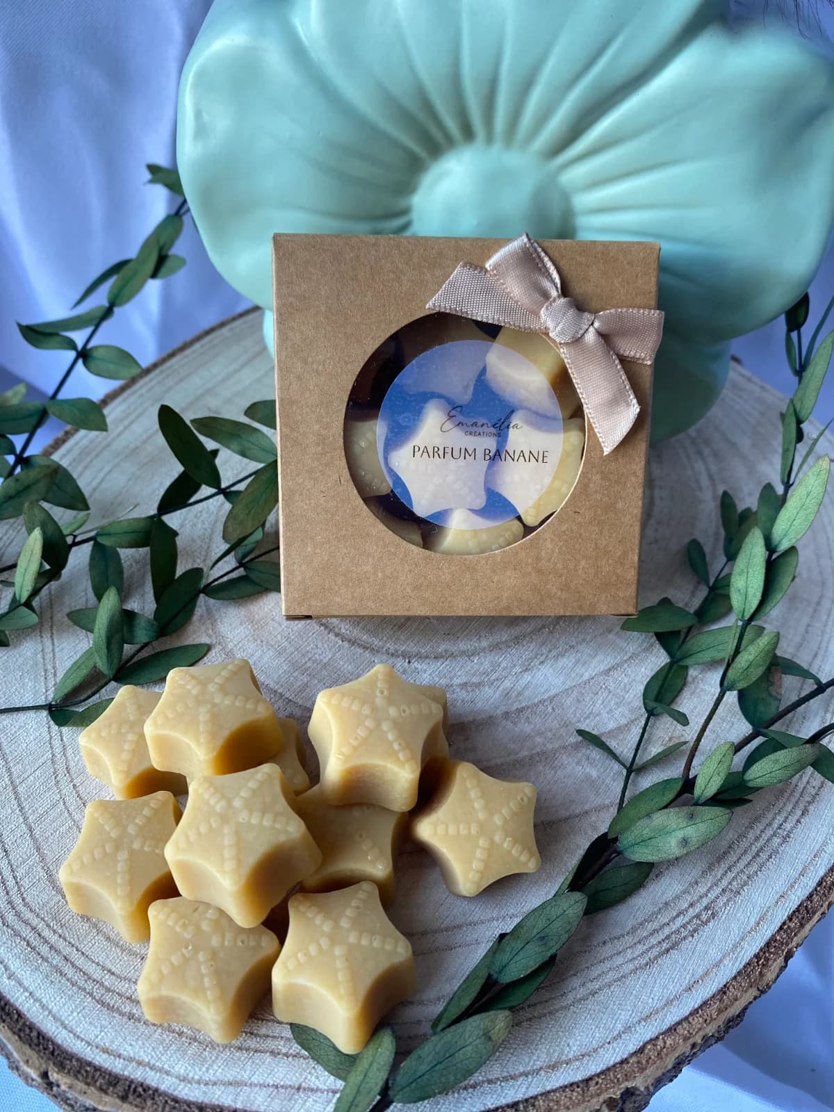 Petits fondants jaunes étoilés disposés devant leur coffret kraft à ruban sur un disque de bois.