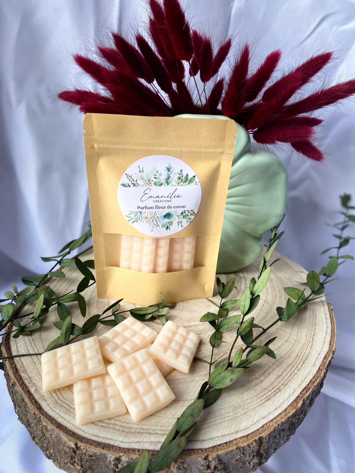 Sachet kraft et fondants parfumés blancs en forme de mini tablettes sur un rondin de bois décoré de feuillage.