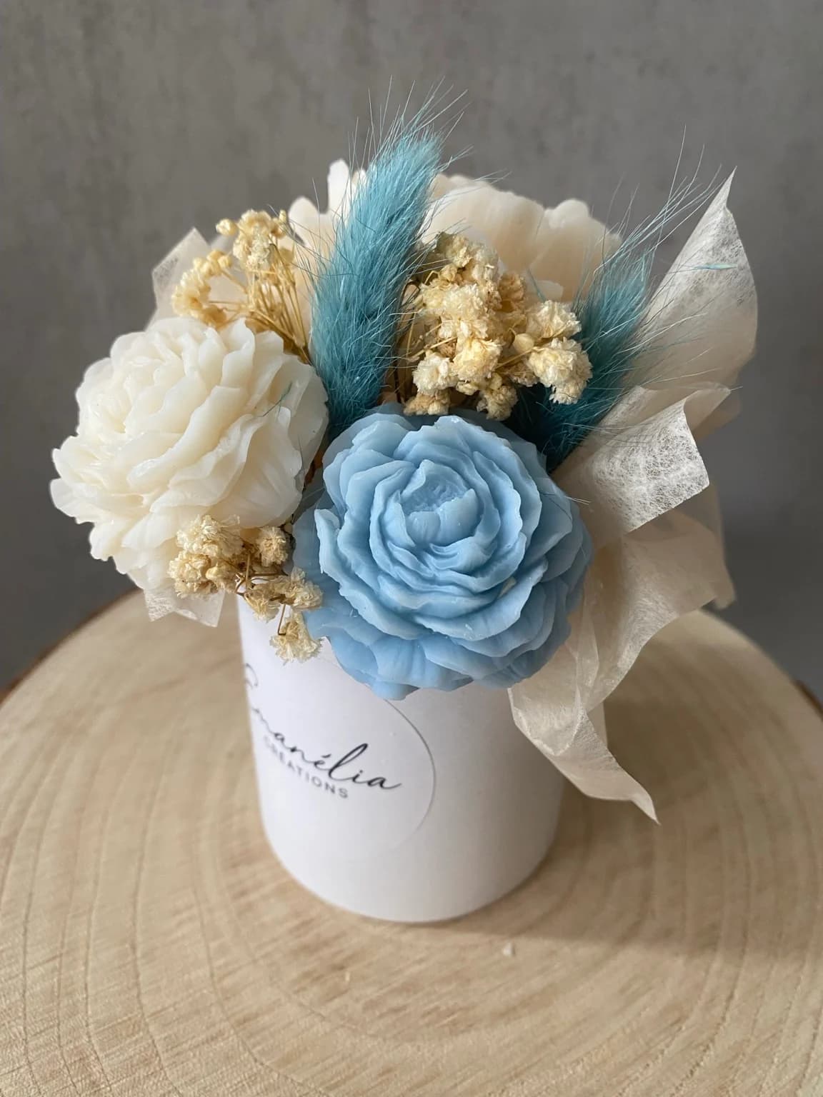 Vue rapprochée du bouquet Céleste aux fleurs de cire ivoire et bleue accompagnées de brins séchés.