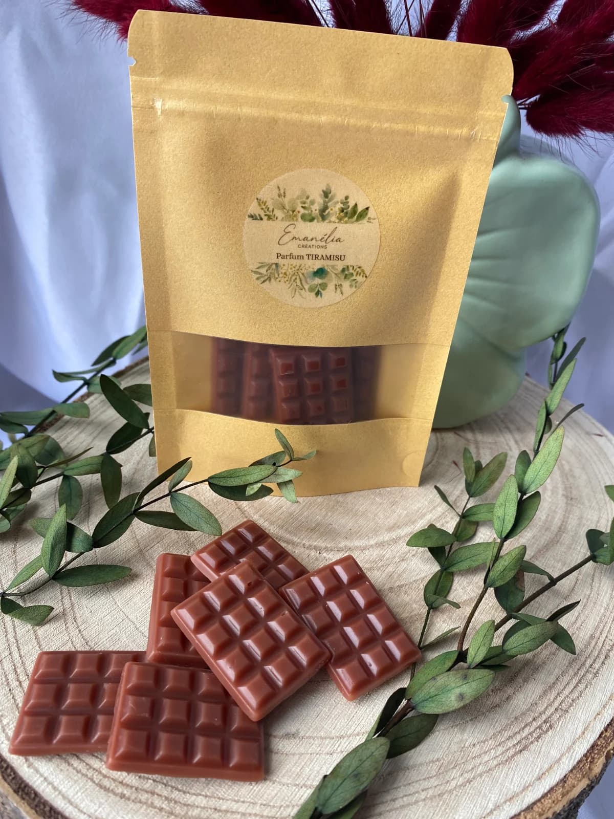 Gros plan sur les fondants parfumés marron façon tablette et leur sachet kraft sur une tranche de bois.