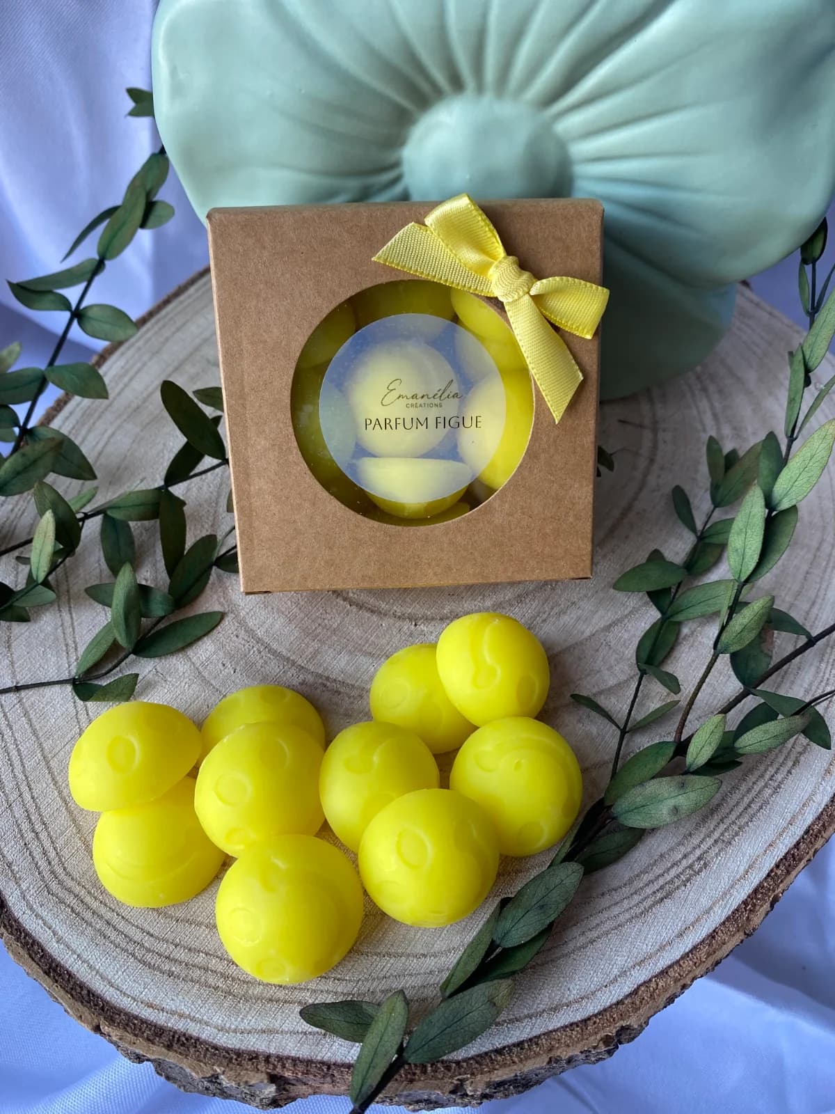 Vue plongeante du coffret kraft à ruban jaune et de fondants smiley jaunes posés sur un disque de bois.