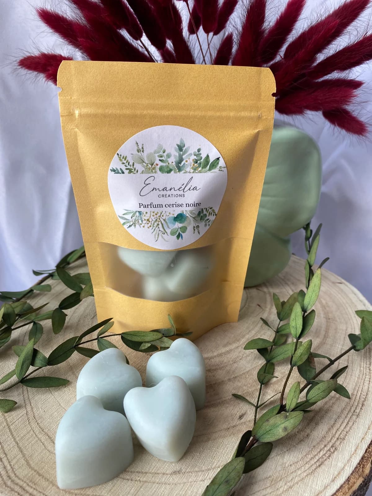 Vue d'ensemble du sachet kraft et des fondants cœurs vert pâle sur tranche de bois avec fleurs séchées.