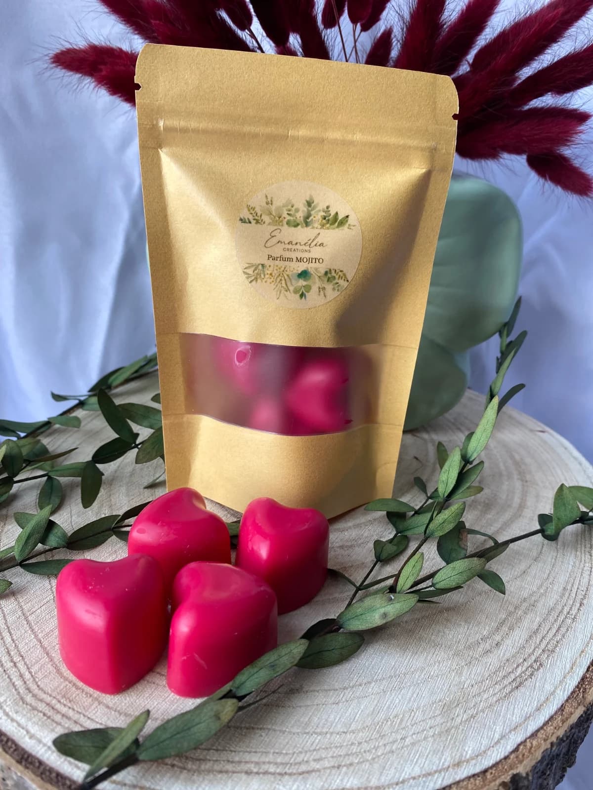 Quatre cœurs fondants rose fuchsia devant leur sachet kraft étiqueté parfum mojito sur socle en bois.