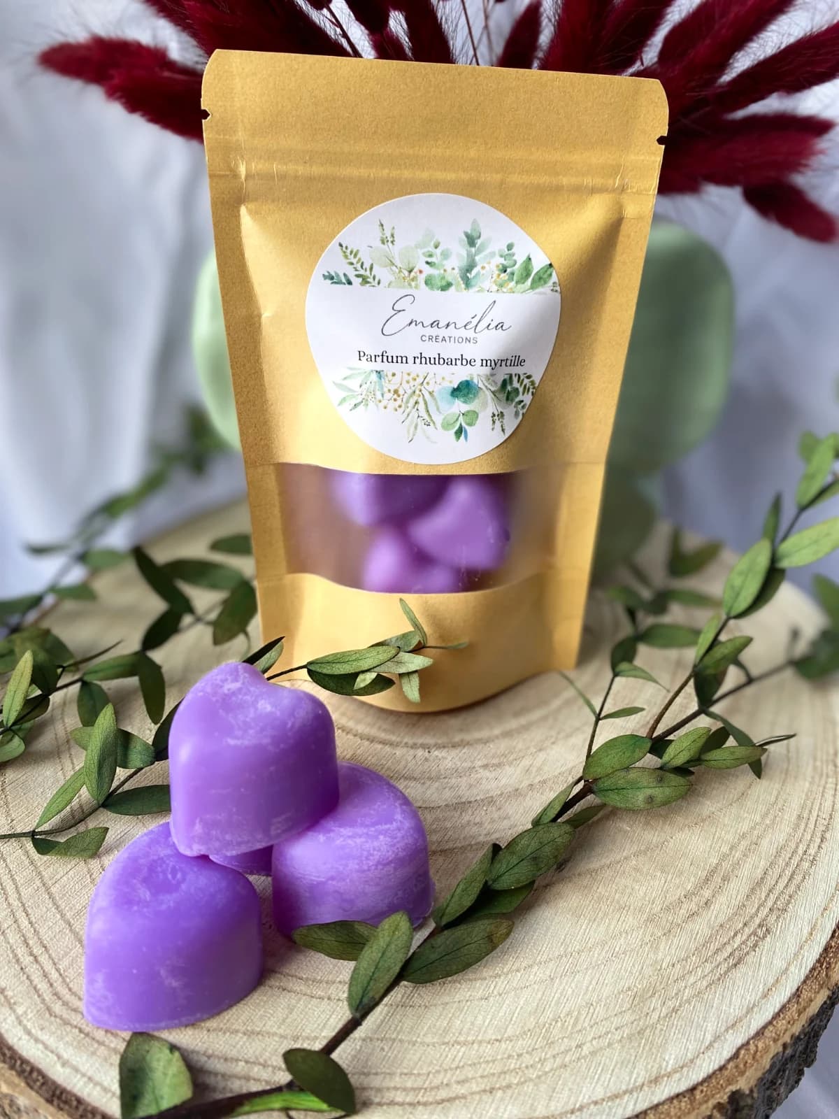 Sachet de fondants et cœurs violets sur un rondin de bois entouré de branchages et plumeaux bordeaux.