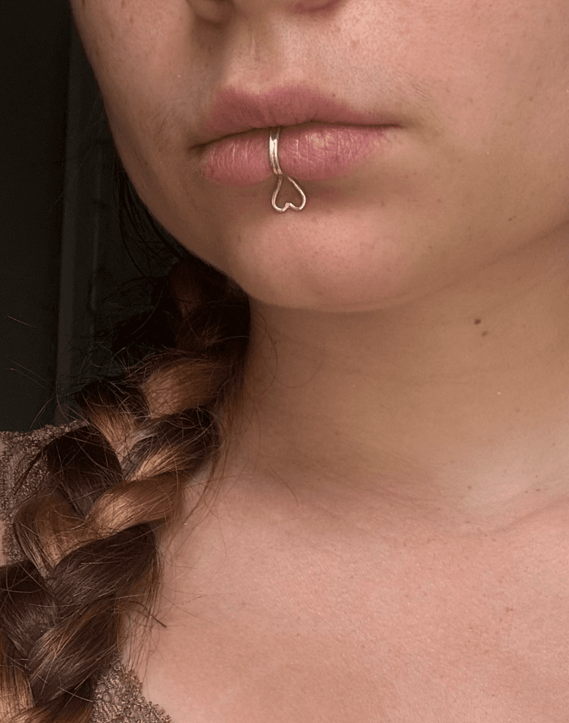 Bague de lèvre en argent avec motif cœur ajouré, portée sur la lèvre inférieure, vue de trois-quarts.