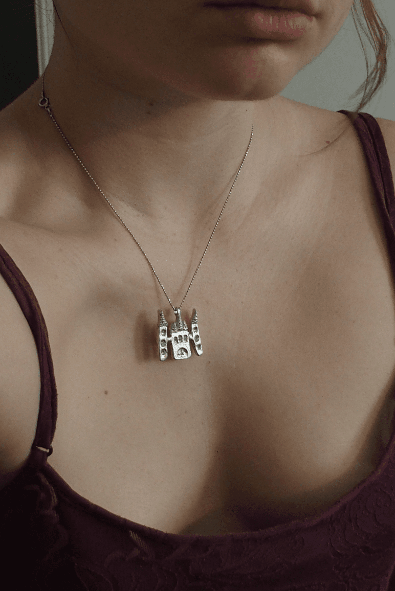 Pendentif en étain en forme de château avec tours porté autour du cou sur une fine chaîne.